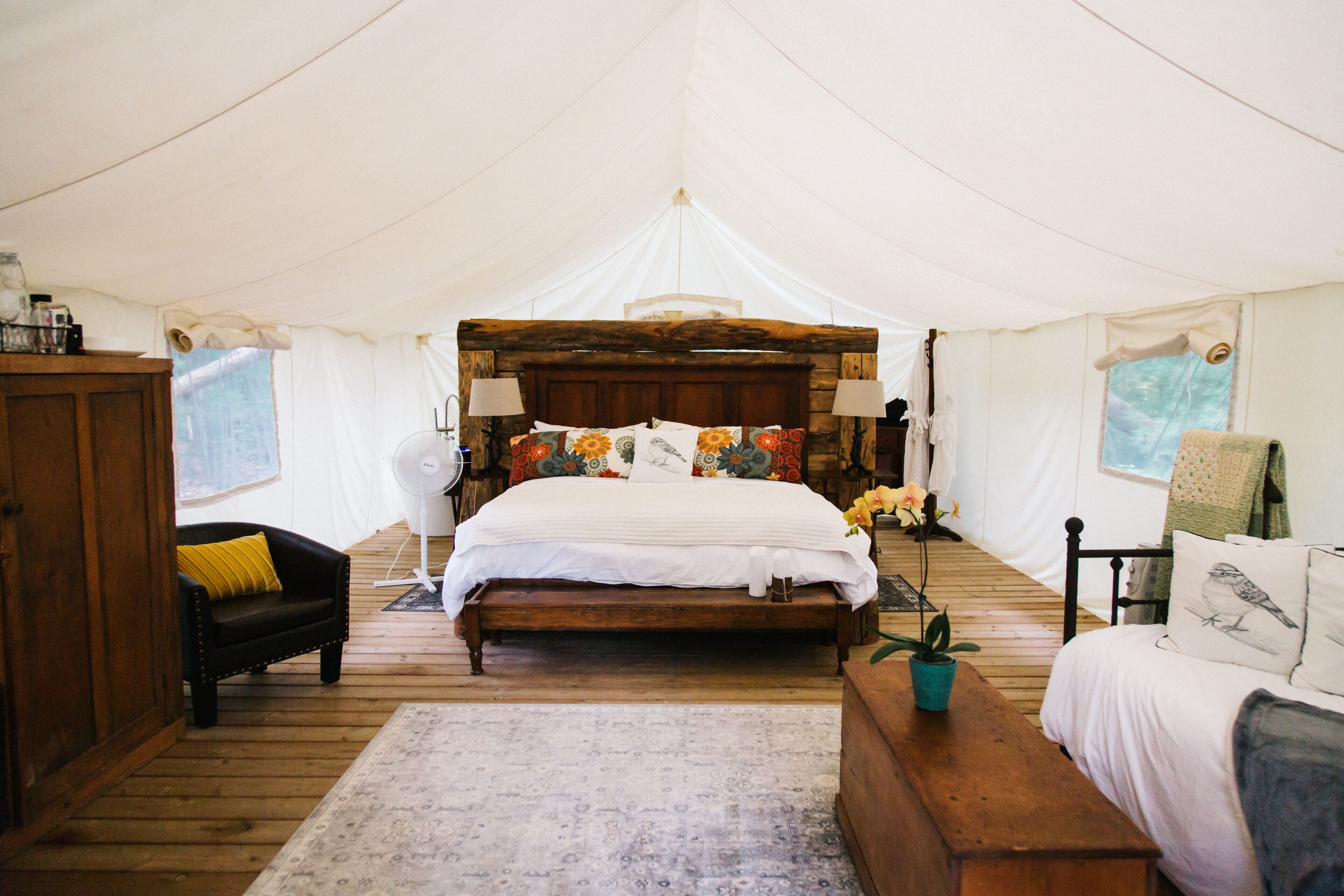 A tented room with a wooden bed, a wooden bench, a small table, and a chair.