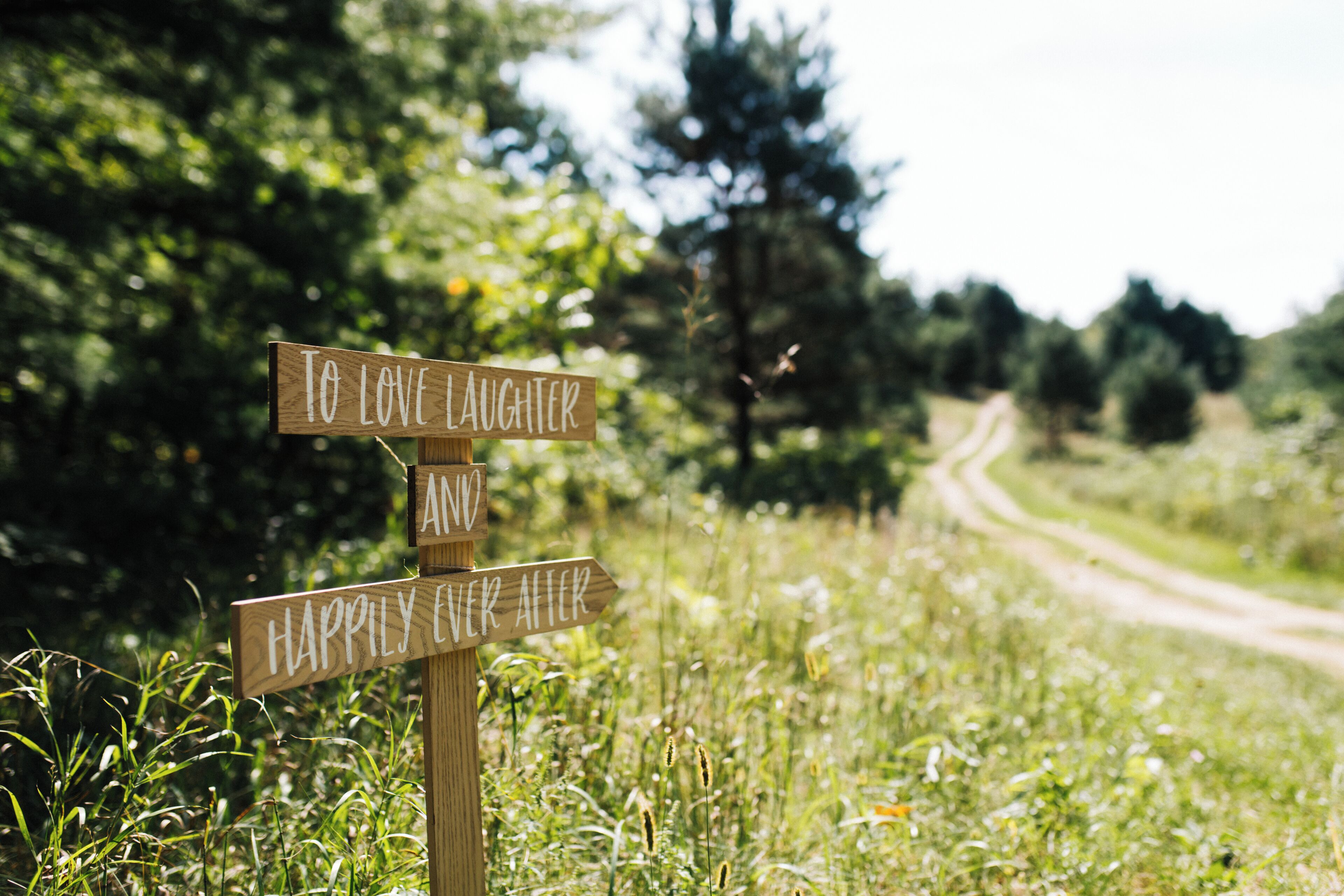 A wooden signpost with two directional signs in a grassy area with a dirt path in the background.