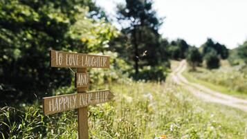 A wooden signpost with two directional signs in a grassy area with a dirt path in the background.