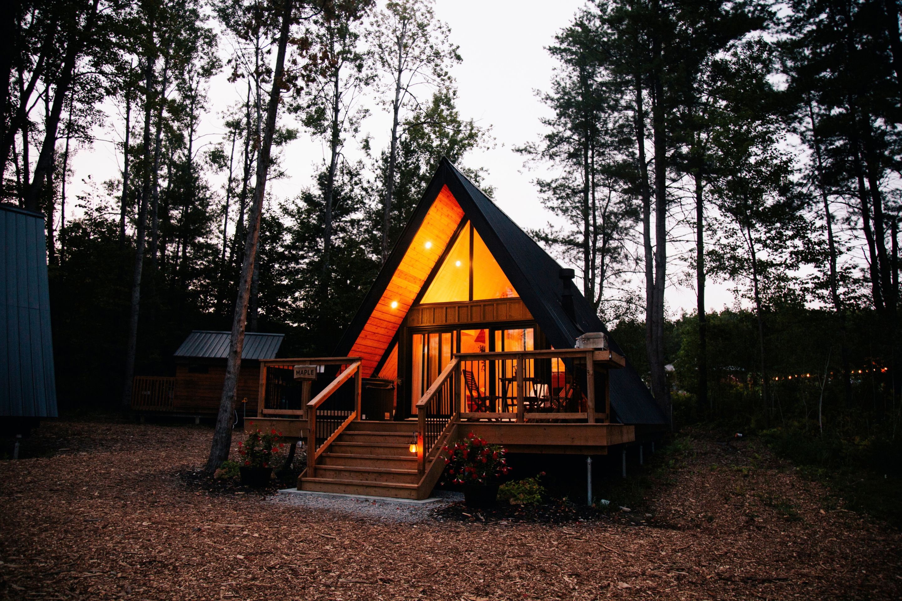 A cabin with a triangular roof, a wooden deck, and a staircase leading to the entrance.