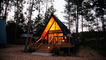 A cabin with a triangular roof, a wooden deck, and a staircase leading to the entrance.