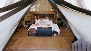 Een gezellig tentverblijf met een houten vloer, een bed met wit beddengoed, een nachtkastje en een kleine plant in een pot.