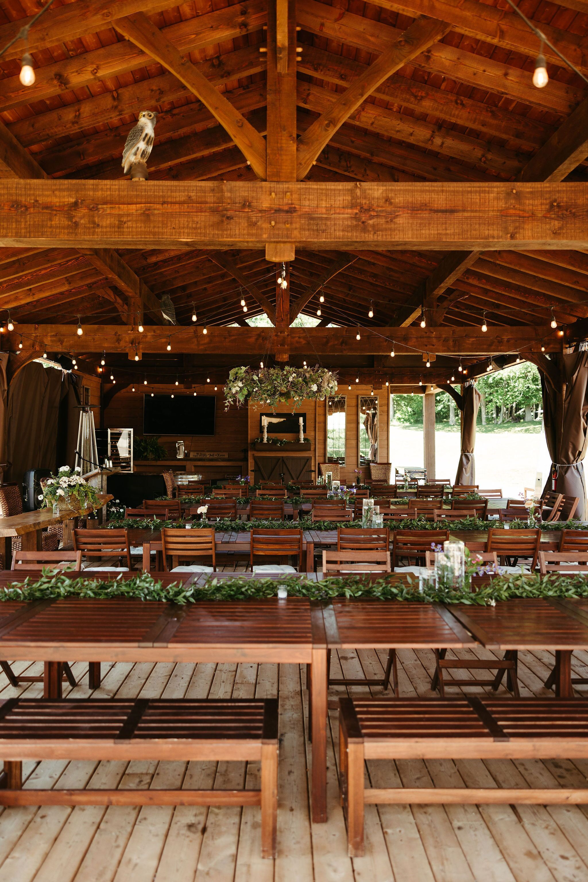 A rustic wooden interior with tables and benches, a hanging light fixture, and a television mounted on the wall.