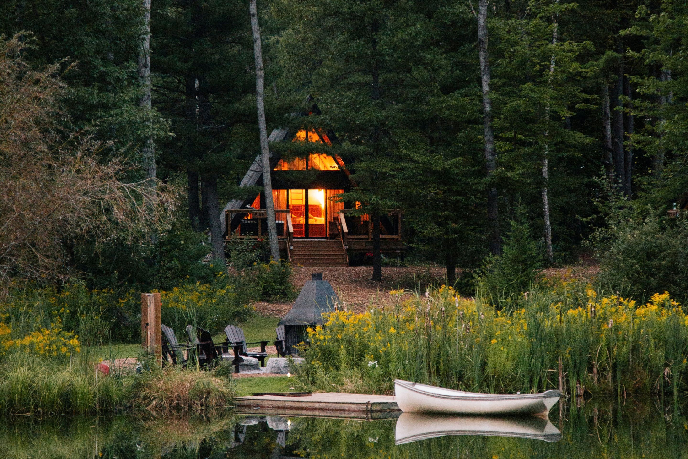 A cabin with a wooden deck, surrounded by a forest and a body of water.