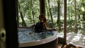 Iemand zit in een bubbelbad met uitzicht op een bos door een groot raam.
