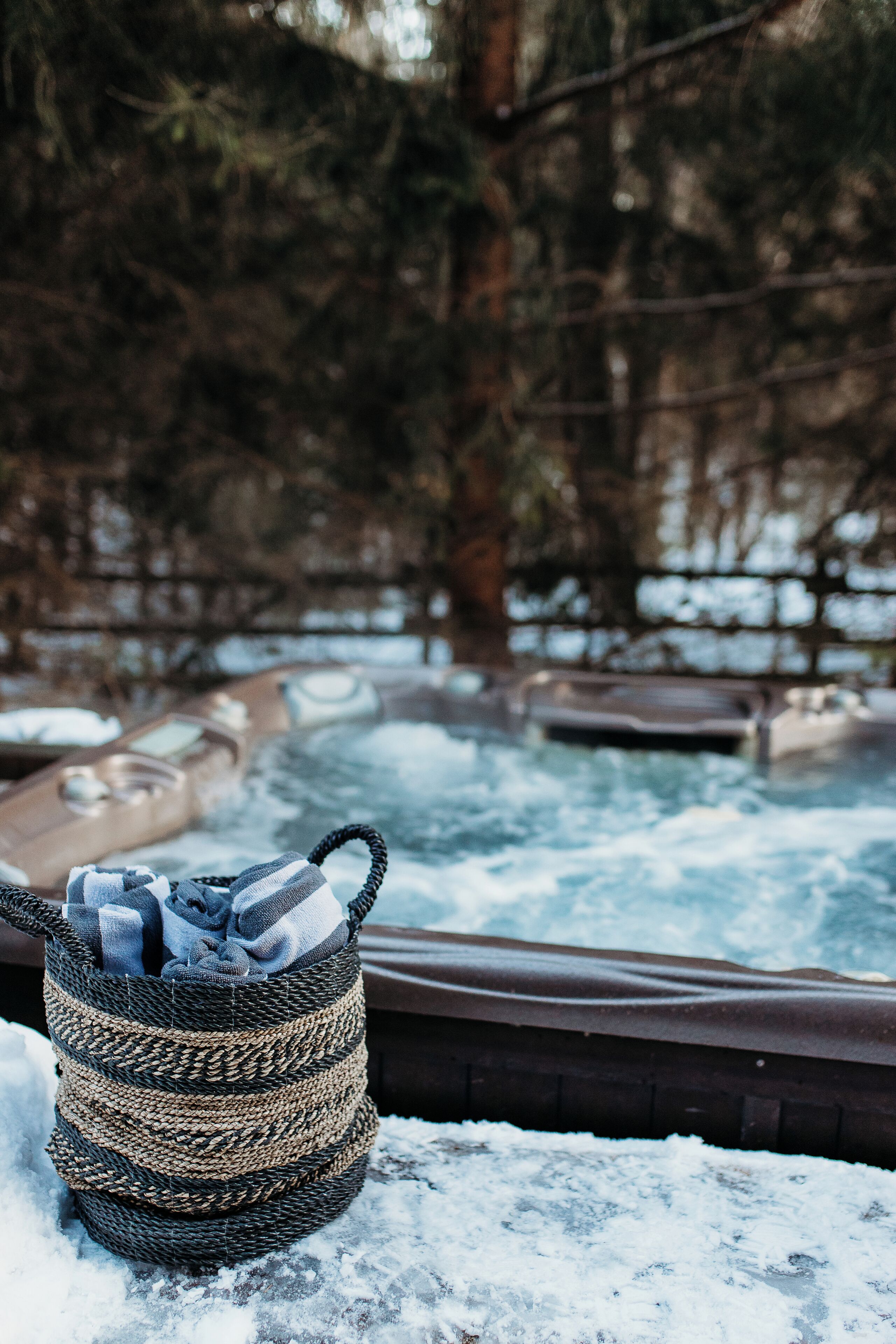 Un jacuzzi rodeado de nieve, con una cesta tejida que contiene objetos sobre el suelo cubierto de nieve.