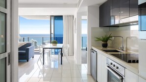 A modern kitchen with a large island, a dining area with a view of the ocean, and a balcony with a sofa and table. - H Residences Ocean View (Surfers Paradise)