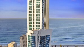 A modern hotel with a unique architectural design, featuring a prominent Hilton sign, located near a beach with a view of the ocean. - H Residences Ocean View (Surfers Paradise)
