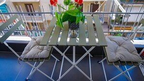 A balcony with a small table, two cushions, and a potted plant with red flowers. - LK apartments A - Athens city (ATHENS)