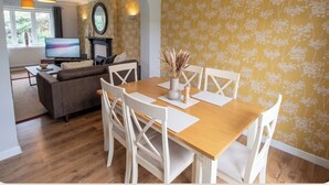 Un comedor con una mesa de madera y sillas blancas, un sofá y un televisor al fondo.