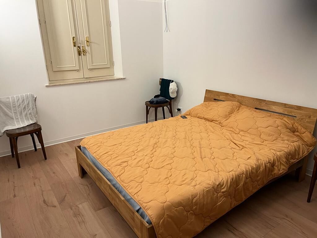 Un dormitorio con una cama de madera, una silla, una mesita y una ventana con cortina.