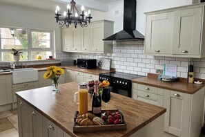 A modern kitchen with white cabinets, a wooden countertop, a black stove, and a chandelier. - Porthcawl Magnificent 7 Bedroom House (Porthcawl)