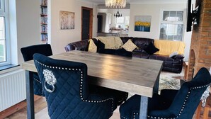 A dining area with a wooden table and upholstered chairs, a sofa with cushions, a bookshelf, and a chandelier. - Build your memories, hot tub, garden, sleeps 14 (Porthcawl)