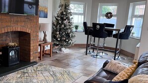 A living room with a fireplace, a Christmas tree, a chandelier, a leather sofa, and a dining area. - Build your memories, hot tub, garden, sleeps 14 (Porthcawl)