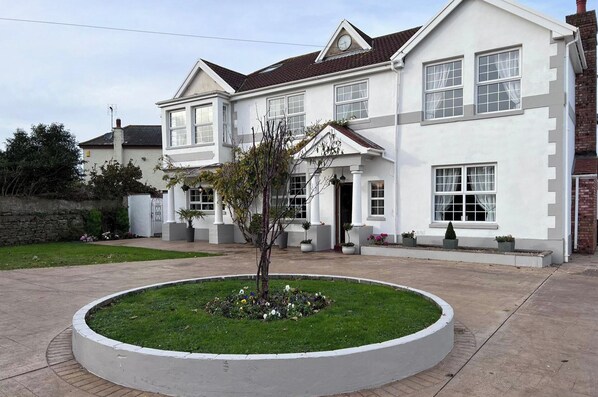 A two-story house with a white exterior, a front porch, and a circular garden with flowers.