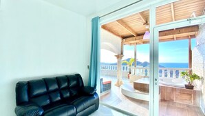A black leather sofa in a bright room with a large sliding glass door leading to an outdoor terrace with a view of the sea. - Inviting 2-Bed Apartment in Cofresi (Cofresi, Puerto Plata)