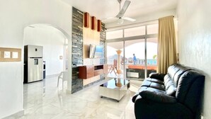 A modern living room with a black leather sofa, a glass coffee table, and a stone accent wall. - Inviting 2-Bed Apartment in Cofresi (Cofresi, Puerto Plata)