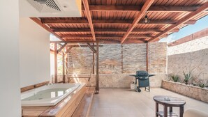 Un patio cubierto con un jacuzzi, una mesa y una zona de barbacoa.