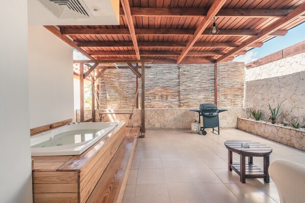 A covered patio with a hot tub, a table, and a grill area.