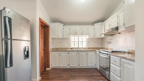 Una cocina con armarios blancos, un refrigerador de acero inoxidable, horno empotrado y encimera de granito.