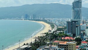 Un paysage urbain côtier avec un grand hôtel qui domine l’horizon, une plage et une montagne en arrière-plan.
