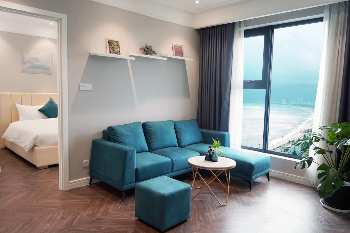 A modern living room with a teal sofa, a round coffee table, and a view of the ocean.