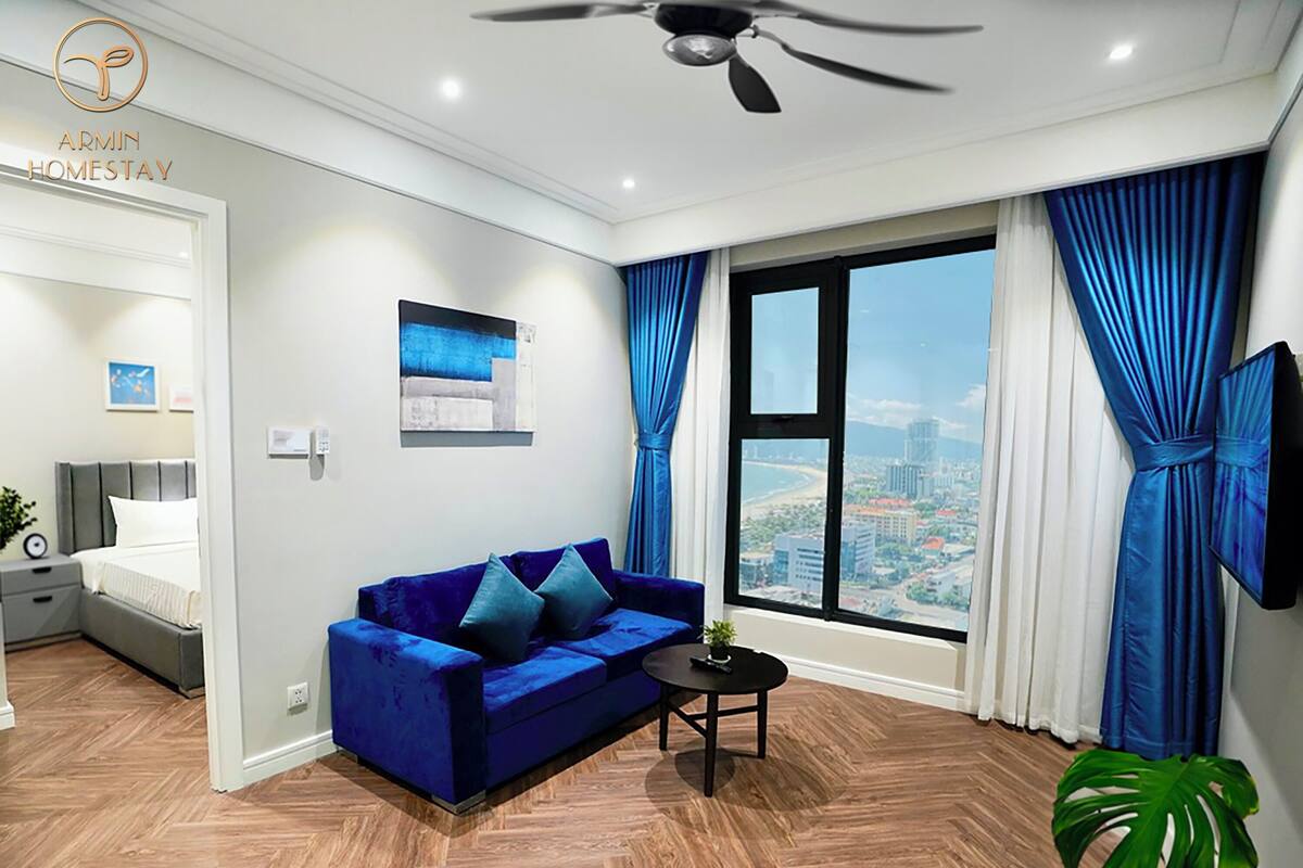 A modern living room with a blue sofa, a small round table, and a city view through large windows.
