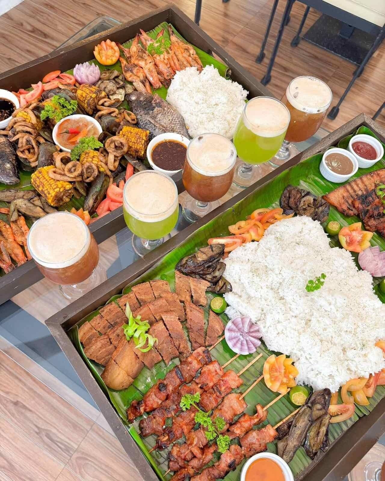 A large dining table with various dishes, including grilled meats, seafood, and rice, along with several drinks.