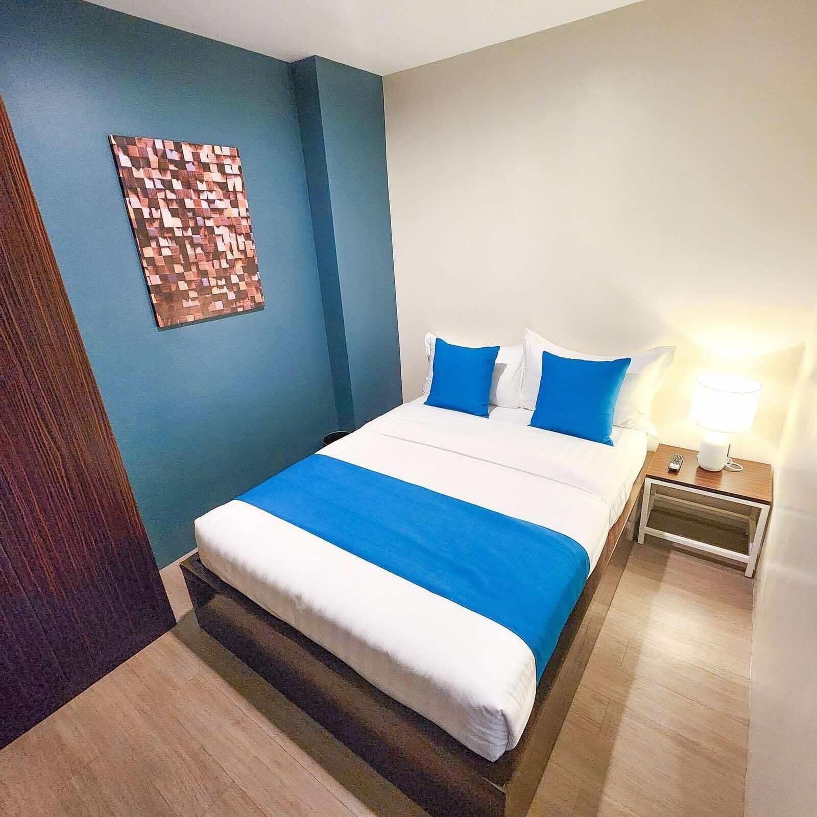 A neatly made bed with blue and white bedding, a small bedside table with a lamp, and a wall art piece.