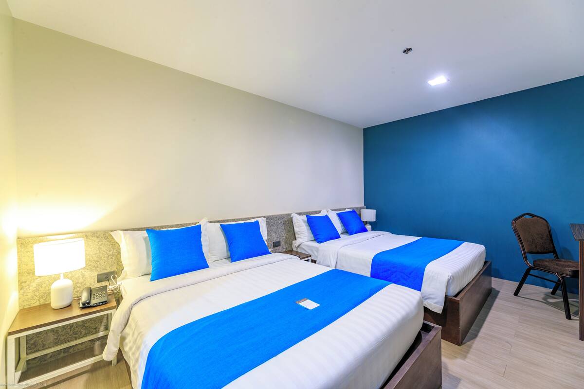 A hotel room with two beds, a desk with a lamp, a chair, and a nightstand with a phone.
