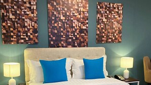 A hotel room with a bed, two bedside tables, a lamp, a chair, and three wall art pieces. - Fynn Boutique Hotel (Bacoor City)