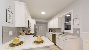 Une cuisine moderne avec des meubles blancs, un îlot central doté de deux éviers et de serviettes, et un tapis à motifs.