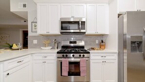 Une cuisine moderne avec des meubles blancs, des appareils en acier inoxydable et un dosseret carrelé.