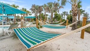 Une zone de plage aménagée avec des hamacs, une piscine et des palmiers.