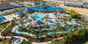 Vista aérea de un complejo turístico con varias piscinas, palmeras y un edificio grande con techo azul.