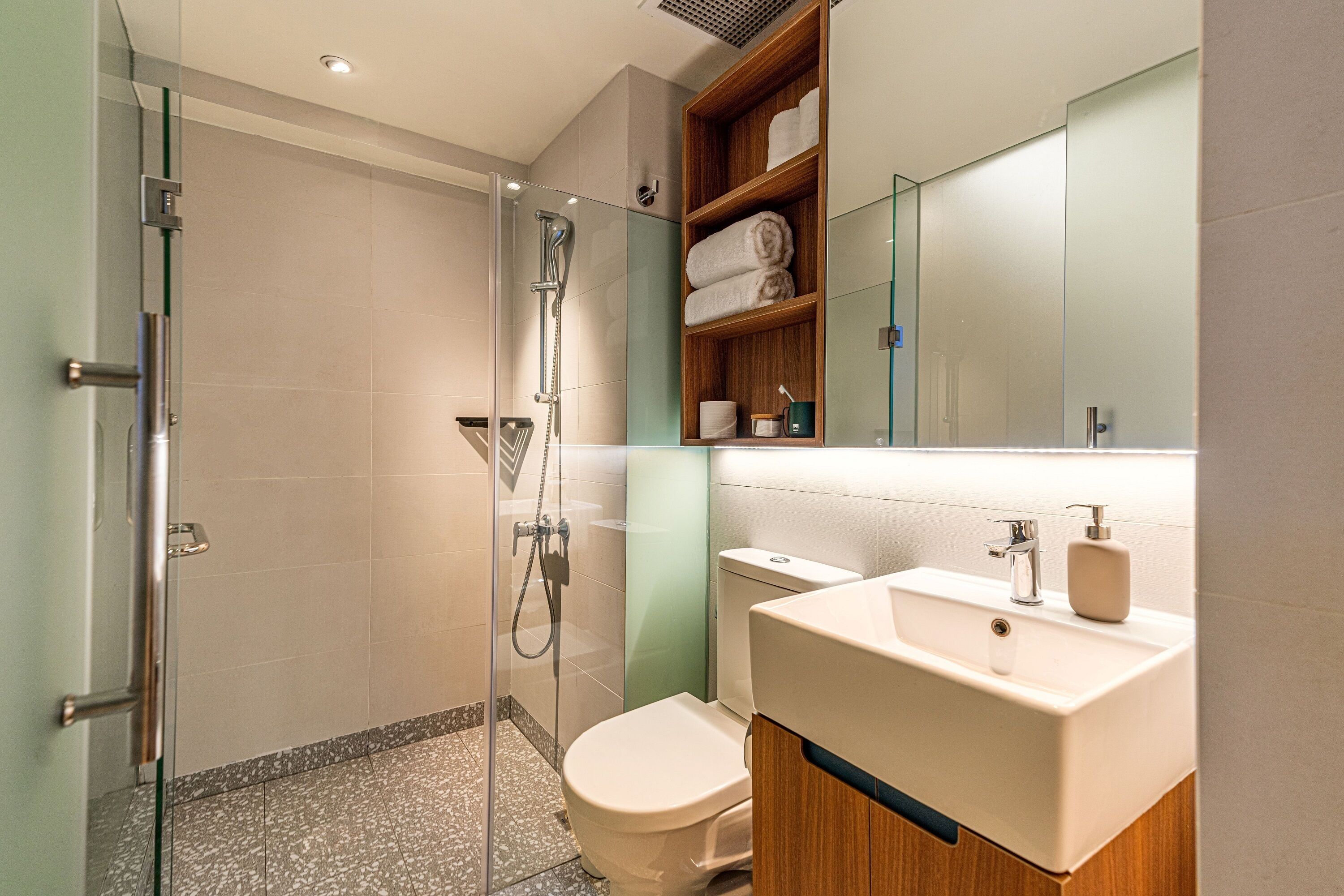 A modern bathroom with a glass-enclosed shower, a white toilet, and a wooden vanity with a sink and mirror.