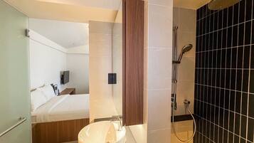 Un baño moderno con un lavamanos grande, ducha y una cama a la vista en el fondo.
