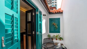 A narrow outdoor corridor with teal doors and shutters, a small table with a chair, and potted plants. - Weave Suites - Midtown (Singapore)