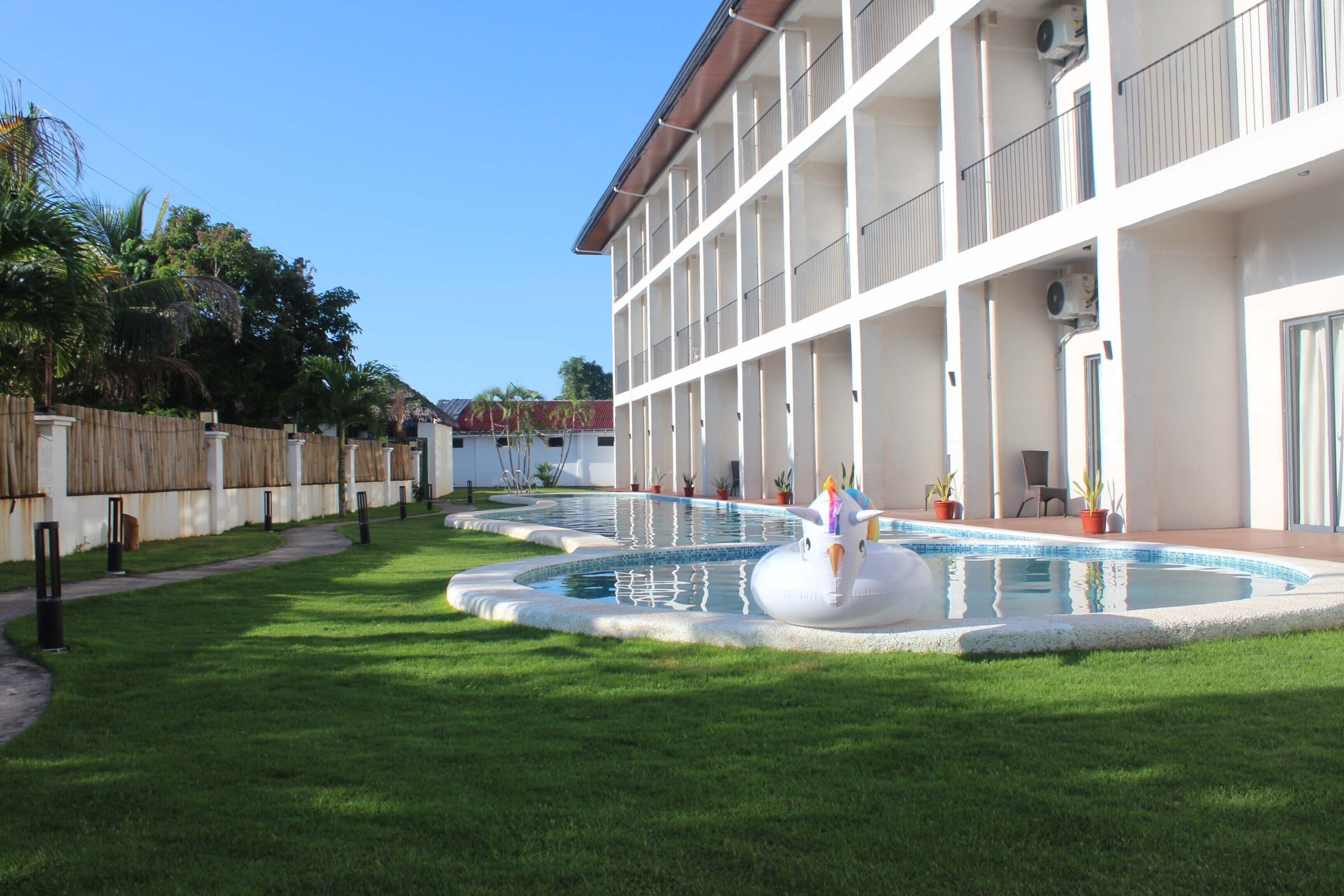 A hotel with a pool area, multiple balconies, and a well-maintained lawn.