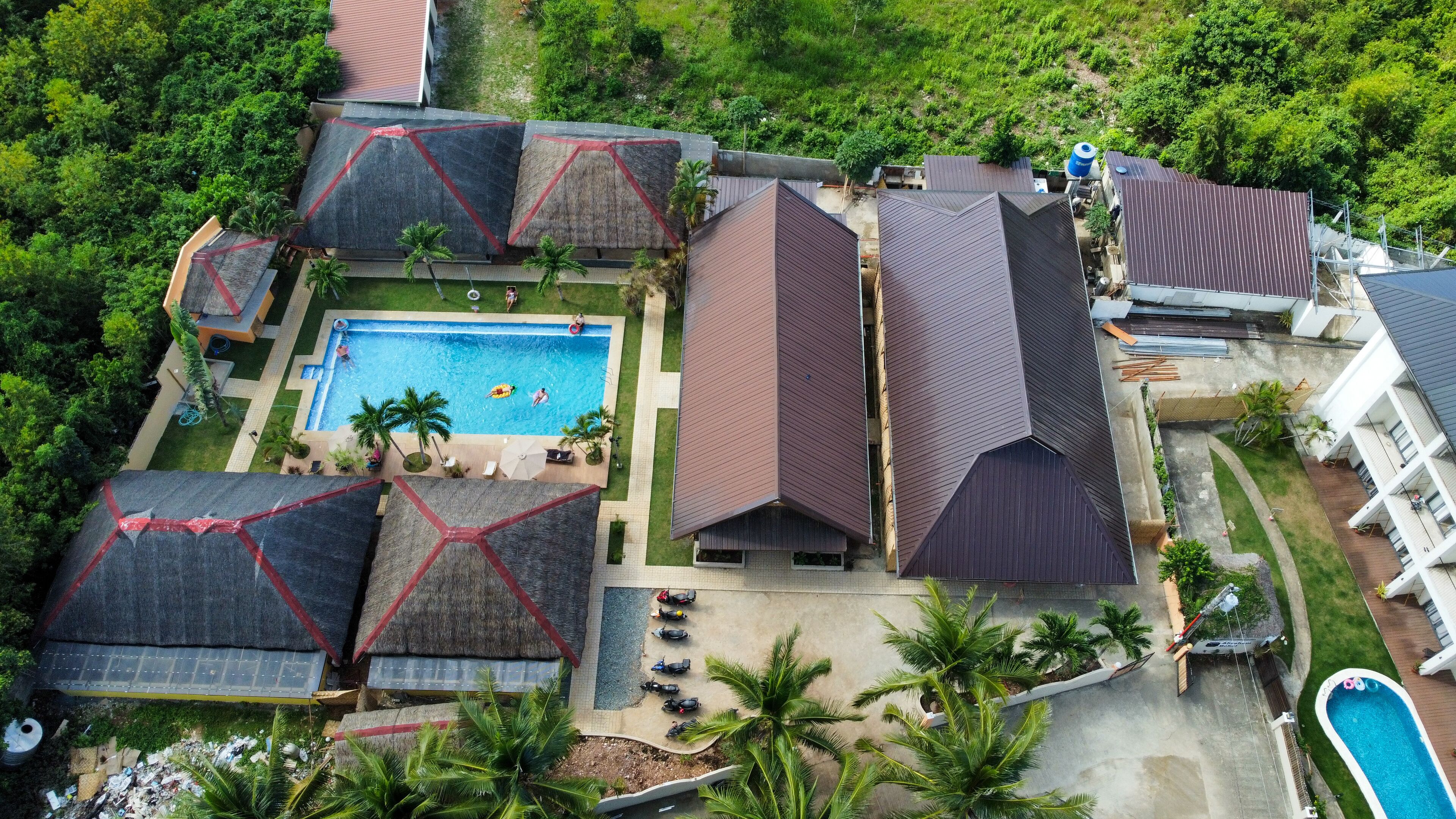 An aerial view of a resort with multiple buildings, a swimming pool, and surrounding greenery.