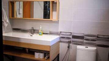 A bathroom with a wooden vanity, a mirror, a sink, a toilet, and a shower.