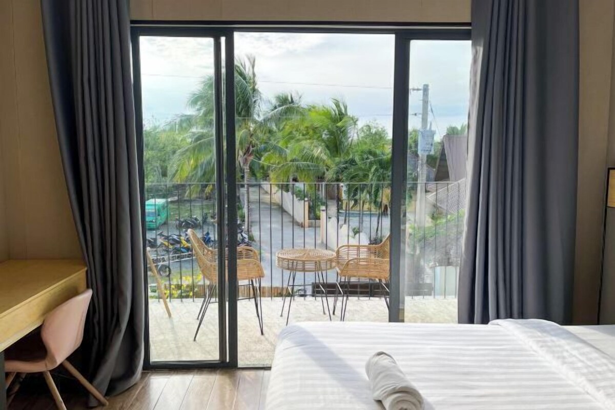 A room with a bed, a desk, and a balcony with chairs and a table.
