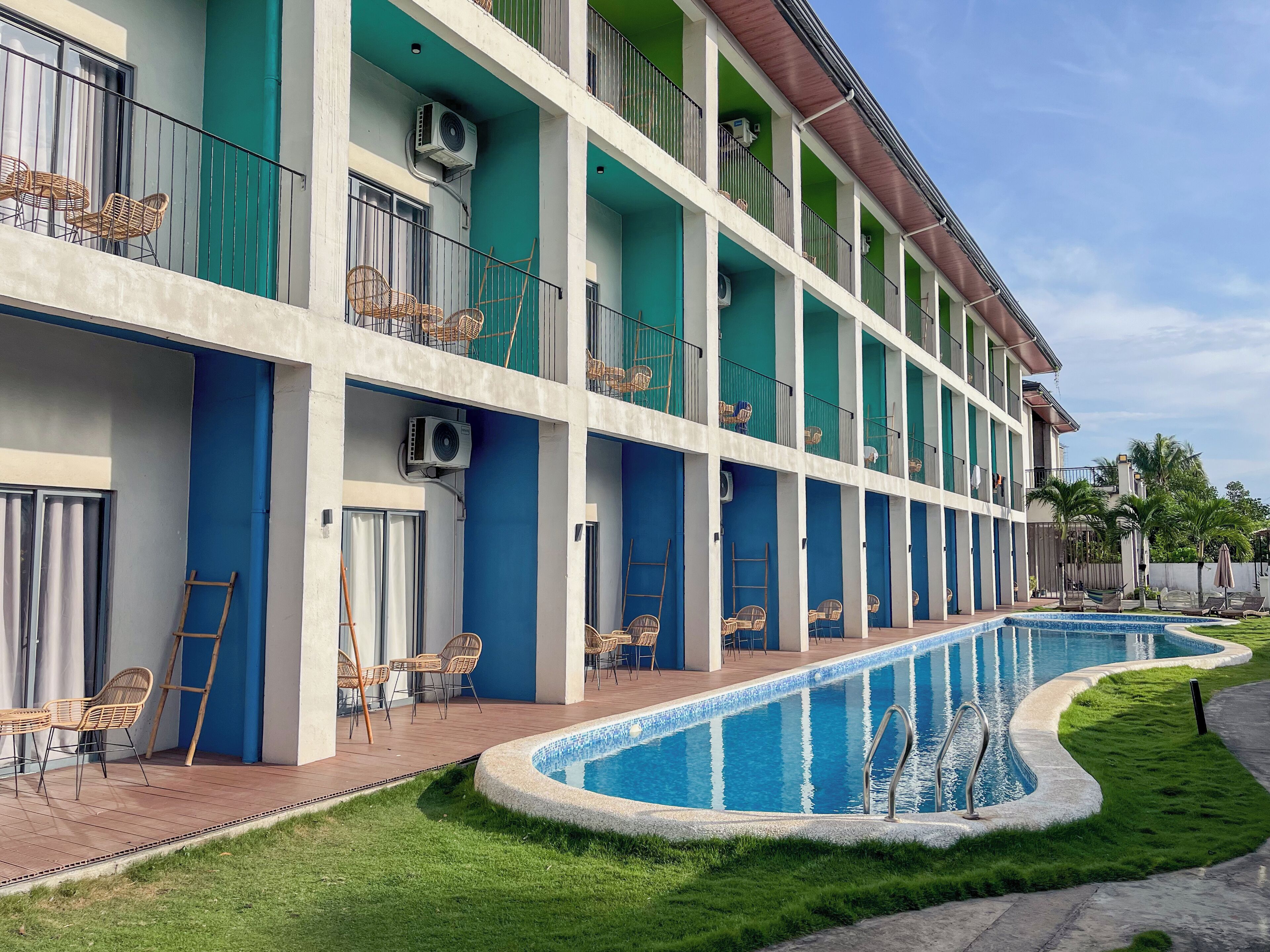 A multi-story hotel with a swimming pool, outdoor seating, and air conditioning units.
