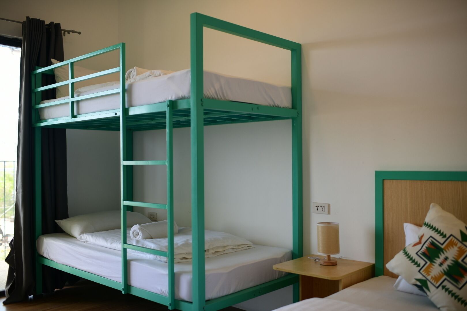 Habitación con literas, una mesita de noche con lámpara y ventana con cortinas.