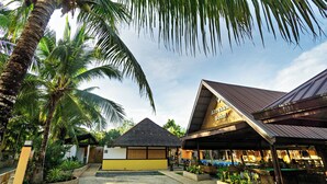 Un resort tropical con un edificio de techo de paja, un área de estar al aire libre cubierta y exuberante follaje.