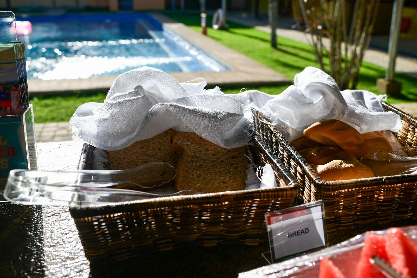A breakfast setup with bread baskets and a sign labeled "BREAD" near a pool.