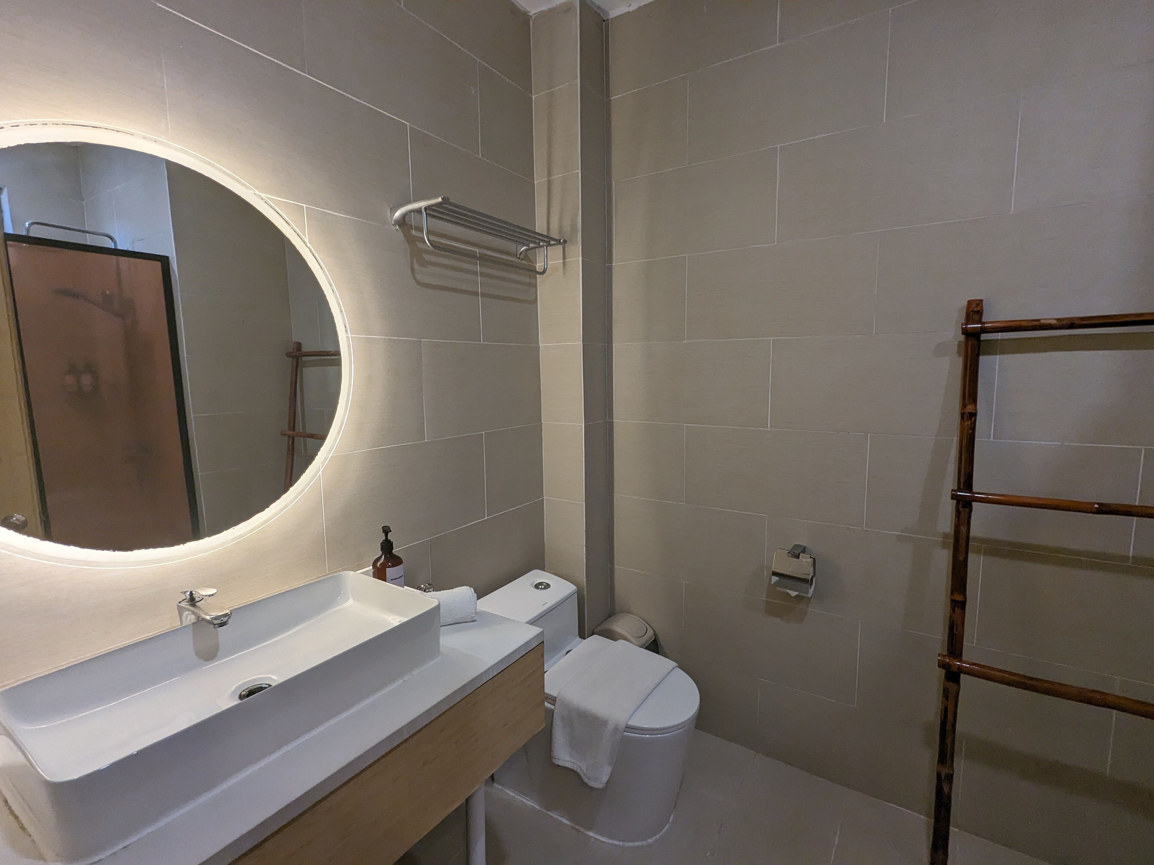 A bathroom with a white sink, a mirror with a light, a toilet, and a towel rack.