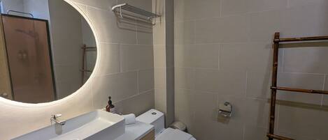 A bathroom with a white sink, a mirror with a light, a toilet, and a towel rack.