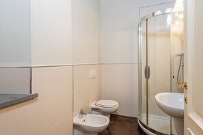 Un baño con inodoro, bidé y zona de ducha con mampara de vidrio.