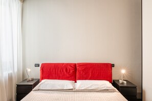 Una habitación de hotel ordenada con una cama, dos mesitas de noche y un buró con una lámpara.